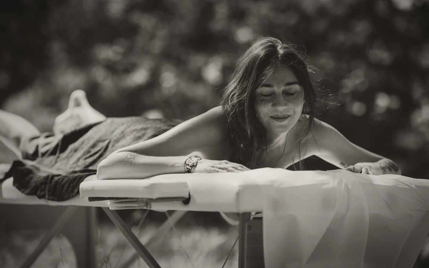 A guest lying face down on a massage table outdoors, eyes closed, smiling.