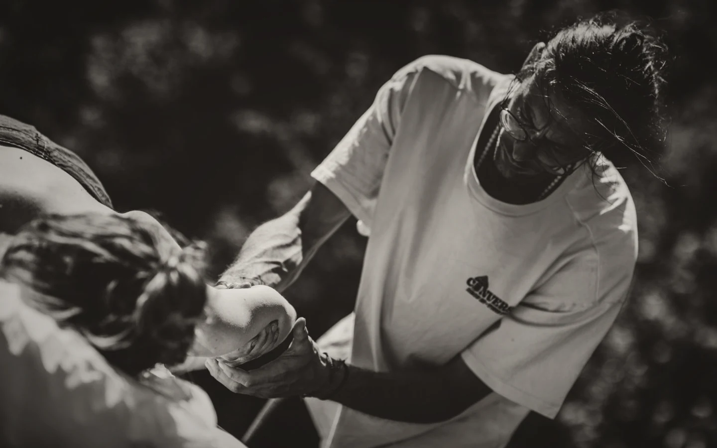 Black and white photograph of hands cradling a guest's head during a massage outdoors.
